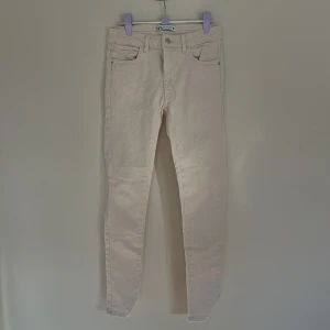 Beige skinny jeans från Zara - Snygga beige skinny jeans från Zara med klassisk femficksdesign och hög midja. Byxorna är i stretchigt bomullsmaterial och har smal passform hela vägen ner. Perfekta för en clean och stilren look.