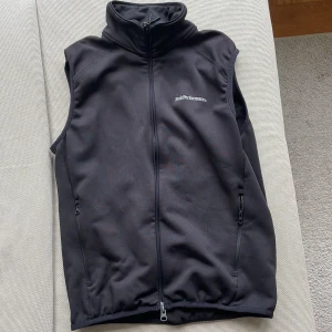 Svart väst från Peak Performance - Svart väst från Peak Performance med hög krage och hel dragkedja framtill. Västen har två fickor med dragkedja och broderad logga på bröstet. Tillverkad i mjukt syntetmaterial, perfekt för lager-på-lager och outdoor.