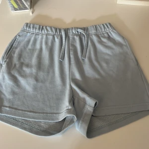 Ljusblå shorts från KIDSONLY - Ljusblå mjuka shorts från KIDSONLY med elastisk midja och snörning. Shortsen har två sidofickor och är tillverkade i bomullsmaterial med meshfoder på insidan. Perfekta för varma dagar eller chill hemma.