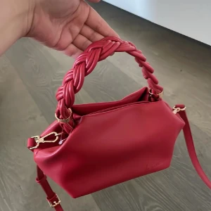 Snyggaste väskan❤️ - Snygg röd handväska från k.cobler i skinn med justerbar axelrem och ett unikt flätat handtag. Väskan har guldiga metalldetaljer och en stilren, mjuk form. Perfekt för dig som vill sticka ut med en färgstark accessoar. Använd gärna köp nu❤️