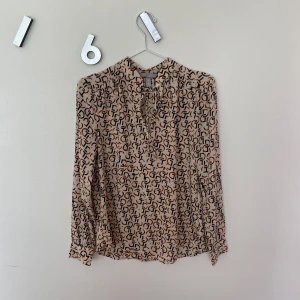 Brun / beige blus från H&M - Beige blus med bruna detaljer och knytning vid halsen. 