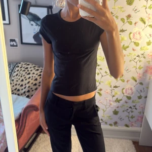 Svart croppad t-shirt - Enkel svart croppad t-shirt med rund hals och korta ärmar. Sitter tight och har en clean look som passar till allt. Mjuk och stretchig känsla, perfekt till jeans eller kostymbyxor.