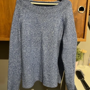 Blå stickad tröja med rund hals - Mysig blå stickad tröja med melerad look och rund halsringning. Tröjan har långa ärmar och ribbade muddar vid ärmslut och nederkant. Perfekt för lager-på-lager och chill dagar.