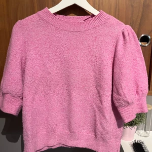 Rosa stickad tröja med puffärm - Superfin rosa stickad tröja med puffiga ärmar och ribbade muddar. Tröjan har en rund halsringning och är gjord i ett mjukt material som känns skönt mot huden. Perfekt för dig som vill ha en söt och trendig look med lite volym på axlarna.