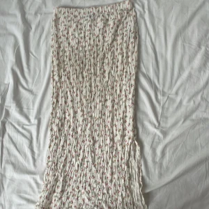 Vit blommig långkjol med slits - Supersöt vit långkjol från mango!  Kjolen har små blommor i rosa, orange och grönt och en slits på sidan. Köpt förra sommaren och är i gott skick Storlek: xs