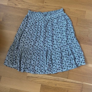 Svartvit blommig kjol med volang - Supersöt svartvit kjol med blommigt mönster och volang nertill. Resår i midjan gör den bekväm och lätt att bära. Perfekt för dig som gillar en feminin och avslappnad stil.