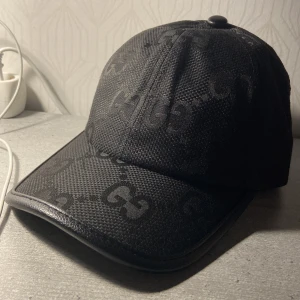 Svart keps Gucci Jumbo keps med GG-mönster - Snygg svart keps från Gucci med klassiskt GG-mönster över hela kepsen. Kepsen har en böjd skärm med läderdetaljer och justerbart spänne bak i svart skinn. Perfekt för dig som vill ha en stilren och lyxig accessoar🙌🏻🤩. Nästan nyskick ✨💯, pris kan diskuteras🤑….Med vänliga hälsningar Ahmad💯🔥 (KEPSEN ÄR LJUSTERBAR alltså passar alla åldrar)🤩