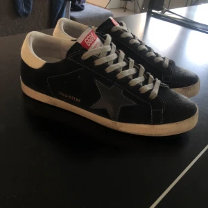 Golden goose skor - Snygga mörkblåa sneakers från Golden Goose med ikonisk stjärndetalj på sidan. Skorna har vit hälkappa, grå snörning och vit sula. Ovandelen är i mocka och detaljer i skinn. Perfekta för dig som gillar streetstyle och vill sticka ut. Allt OG ingår och priset är inte fast så kom med bud✅