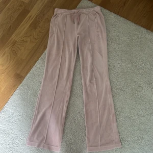 Rosa velourbyxor Juicy Couture S - Supermjuka rosa velourbyxor från Juicy Couture med bootcut-snitt och snörning i midjan. Bak på byxan står det 'Juicy' i glittriga stenar. Perfekta för en chill och trendig look. limited edition 2022.