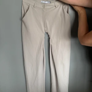 Beige kostymbyxor från 157 XS - Snygga beige kostymbyxor från 157 i storlek XS. Byxorna har raka ben, hällor för bälte och klassisk knappstängning framtill. Perfekta för en clean och stilren look. Materialet känns mjukt och har en lätt stretch för extra komfort.