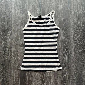 Randig svartvit linnetopp - Snygg randig linnetopp med svarta och vita horisontella ränder. Topp med smala axelband och figurnära passform, perfekt för varma dagar. Enkel och stilren design som funkar till jeans eller shorts.