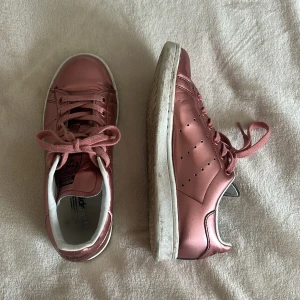 Adidas Stan Smith metallic rosa sneakers - Snygga Adidas Stan Smith sneakers i metallic rosa med vita detaljer och klassisk platt sula. Skorna säljs då dom tyvärr inte används längre. Supersnygga till dig som vill ha en extra detalj på stilen. De är köpta på plick, tyvärr ingen box till dom. De är använda men fortfarande i bra skicka. Säljs för 350 kr, priset går att diskutera vid snabbt köp.🥰💞