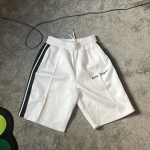 Vita boxing shortsPalm Angels med svarta ränder - Palm Angels vita shorts med svarta sidoränder och broderad logga på vänster ben. Elastisk midja med snörning för skön passform. Sportig look och raka ben, perfekta för en clean och trendig stil.