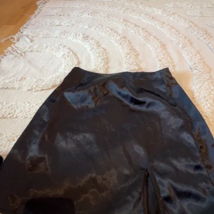 Svart satin kjol  - Snygg svart satin kjol från  i kort modell. Kjolen har en liten slits framtill.