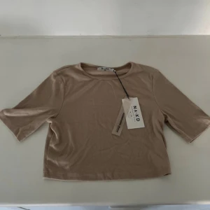 Beige ribbad t-shirt från NA-KD - Snygg beige ribbad t-shirt från NA-KD i croppad modell. T-shirten har korta ärmar och är tillverkad av återvunnet material. Perfekt för dig som gillar stilrena och enkla plagg med en modern touch.