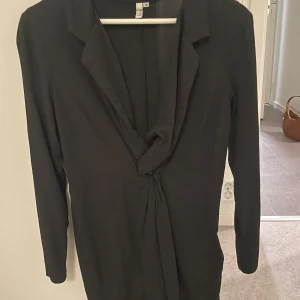 Svart omlottklänning från NLY Trend - Snygg svart omlottklänning från NLY Trend i storlek 36. Klänningen har lång ärm, djup v-ringning och knytdetalj i midjan som ger en cool och stilren look. Perfekt för dig som gillar minimalistisk stil och vill ha något enkelt men ändå trendigt.