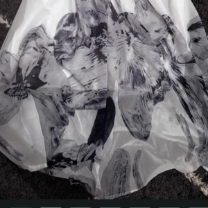 Vit långklänning med blommigt mönster - Säljer en elegant vit långklänning med stora svarta och grå blommor. Klänningen har ett skirt, flowy tyg som ger en lyxig känsla och passar perfekt för speciella tillfällen. Mönstret är riktigt snyggt och ger en cool kontrast mot den ljusa basen.