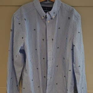 Blårandig skjorta från Ralph Lauren - Snygg blårandig skjorta från Ralph Lauren med broderade små sneakers i grönt och svart över hela plagget. Skjortan har klassisk krage med knappar och är tillverkad i stretchig bomull. Perfekt för dig som gillar preppy stil och coola detaljer.