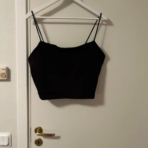 Svart croppad linnetopp från BikBok - Säljer en svart croppad linnetopp från BikBok i storlek XL. Toppen har tunna axelband och en enkel, stilren design som är lätt att matcha med olika outfits. Perfekt för dig som gillar minimalistisk stil och vill ha något bekvämt och snyggt. Katt finns i hemmet 