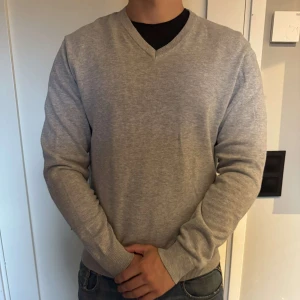Ljusgrå John Henric tröja  - Ljusgrå tröja från John Henric med v-ringad halsring och broderade märken på armbågarna. Toppenskick, knappt använd och har inga märken, skador eller defekter. Storlek S sitter som S/M. Priset ej hugget i sten och accepterar prisförslag, frågor? Bara att höra av sig!