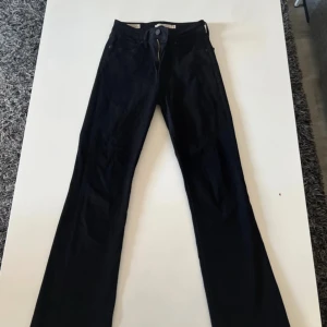 Levi's 725 High Rise Bootcut jeans svart - Snygga svarta Levi's Premium 725 High Rise Bootcut jeans i klassisk bootcut-modell. Hög midja och raka ben med lätt utsvängd passform. Jeansen är tillverkade i ett mjukt bomullstyg med dragkedja och knapp framtill. Perfekta för en cool och tidlös look.