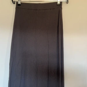 Grå långkjol - Säljer en stilren grå långkjol med ribbad textur. Kjolen har en enkel och elegant design som passar perfekt för olika tillfällen. Den är gjord i ett mjukt och bekvämt material.