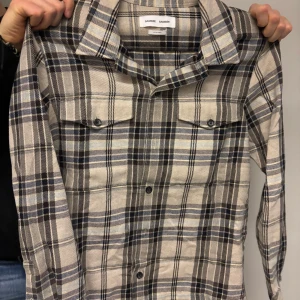 Rutig skjorta från Samsøe Samsøe - Snygg rutig skjorta från Samsøe Samsøe i beige, svart och grått. Skjortan har långa ärmar och knappar framtill. Perfekt för en stilren look.