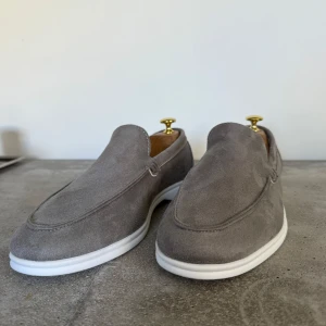 Grå mockaloafers med vit sula - Snygga grå loafers i mocka med en stilren vit sula. Perfekta för en avslappnad men ändå elegant look. Köpta i Frankrike ny pris 900kr mitt pris 499kr