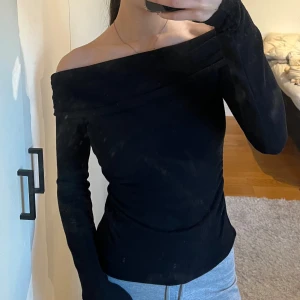 Svart off-shoulder topp från New Yorker - Snygg svart off-shoulder topp med långa ärmar. Perfekt för en stilren look. Passar bra till både jeans och kostymbyxor! Sitter tajt och inte för löst!