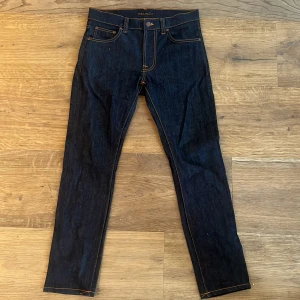 Nudie Jeans - Snygga mörkblå jeans från Nudie Jeans i modellen ”lean dean” med klassisk femficksdesign och kontrasterande orange sömmar. Jeansen har en knappgylf och är tillverkade i ett slitstarkt denimtyg. Perfekta för en stilren look. Storleken är W30 L30 