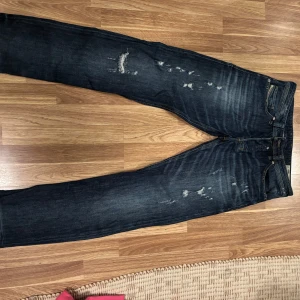 Mörkblå jeans från Diesel - Snygga mörkblå jeans från Diesel med slitna detaljer för en cool look. Modellen är Safado med en regular slim straight passform. Perfekta för en avslappnad stil med en touch av edge. Storlek 32/34 knappt använda