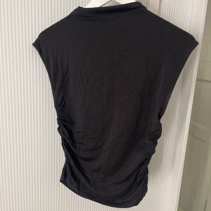 Fin Topp  - Hej! Säljer en stilren svart ärmlös topp från Gina Tricot. Toppen har en tight passform och är tillverkad i ett mjukt material. Har aldrig användts och därför ingen bild där jag bär den, men det är en sån Hedvig hade på sig på en video (se sista bilden). Ber om ursäkt för dålig bild kvalité på sista bilden. Hör av dig vid inresse eller frågor! 💗