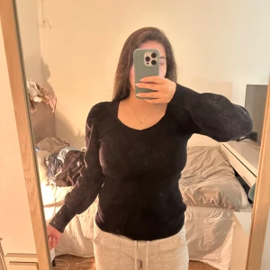 Svart ribbad tröja från vila - Säljer en stilren svart ribbad tröja från vila. Tröjan har en v-ringad design och långa ärmar med en lätt puffig effekt vid axlarna. Perfekt för en elegant och bekväm look.