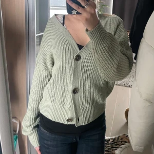 Grön stickad kofta med knappar - Säljer en mysig grön stickad kofta med stora knappar framtill. Koftan har en avslappnad passform och långa ärmar, perfekt för kyligare dagar. Den är enkel att matcha med olika outfits.