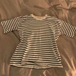 Randig t-shirt - Säljer en klassisk randig t-shirt i vitt och mörkgrönt. T-shirten har en normal passform och korta ärmar, perfekt för en avslappnad stil. Gjord i mjuk bomull för extra komfort.