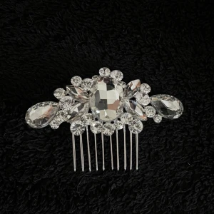 Glittrig tiara - Elegant tiara/hårkam dekorerad med gnistrande strass i olika former och storlekar. Perfekt för att ge en extra touch av glamour till din frisyr. Kammen har en silverfärgad bas som ger en lyxig känsla.