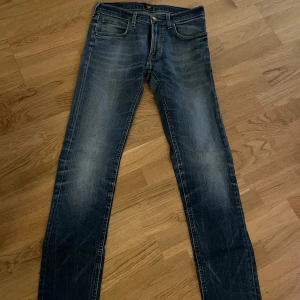 Mörkblå jeans från Lee - Snygga mörkblå jeans från Lee med en klassisk femficksdesign. De har en lätt slitning för en trendig look och stängs med dragkedja och knapp. Perfekta för en avslappnad stil.