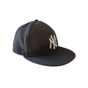 New Era Fitted Keps - Snygg mörkgrå keps från New Era. Storlek 56,8 cm, riktigt snygg och perfekt till sommaren. Tveka inte att höra av dig om du har några frågor!