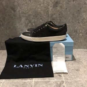 Svarta sneakers från Lanvin - Snygga svarta sneakers från Lanvin med vit sula och klassisk snörning. Perfekta för en stilren look. Skorna kommer med originalförpackning dustbag och kvitto. Sulan är målad en gång därför är priset nedsatt. Tveka inte på att höra av dig. Pris kan diskuteras vid snabb affär.