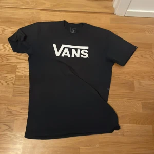 Svart t-shirt från Vans - Säljer en klassisk svart t-shirt från Vans med deras ikoniska logga i vitt på bröstet. Perfekt för en avslappnad stil. T-shirten har en normal passform och är kortärmad.