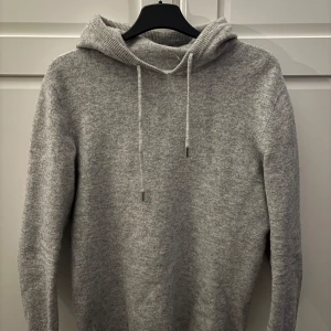 Grå stickad hoodie från NA-KD - Mysig grå stickad hoodie från NA-KD med justerbar dragsko i huvan. Perfekt för kyliga dagar med sin mjuka och bekväma passform. En stilren och enkel design som passar till det mesta.