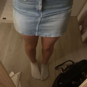 Jeanskjol i ljusblå denim - Snygg kort jeanskjol i ljusblå denim med slitna detaljer. Kjolen har en klassisk femficksdesign och stängs med dragkedja och knapp framtill. Perfekt för en avslappnad stil.