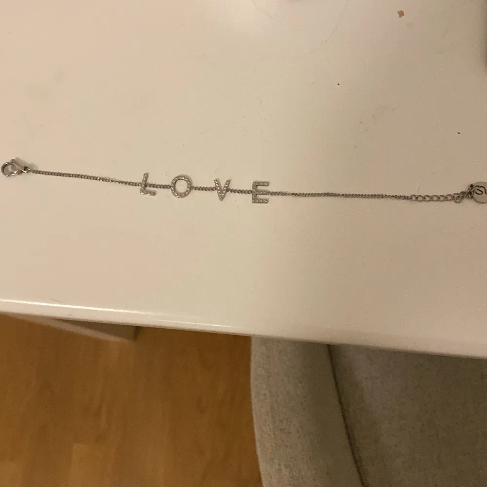 Elegant silverarmband med texten 'LOVE' i glittriga bokstäver. Perfekt för att ge en subtil men stilfull touch till din outfit. Armbandet har en tunn kedja och är lätt att bära.. Asusteet.