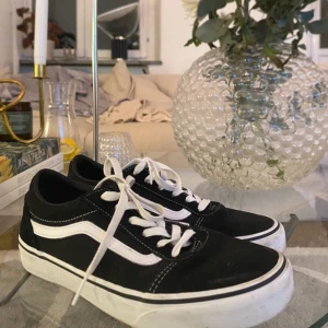 Svarta och vita sneakers från Vans - Säljer ett par klassiska svarta och vita Vans sneakers med den ikoniska sidostripen. Skorna har snörning och en bekväm passform, perfekt för vardagsbruk. Nästan som nya! 