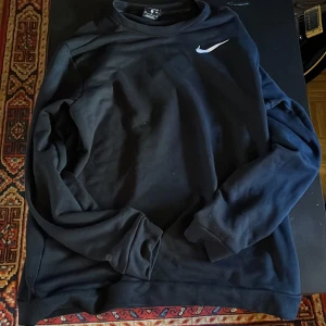 Träningströja från Nike - Säljer en svart tröja från Nike med Dri-Fit teknologi. Tröjan har en enkel design med en vit Nike-logga på bröstet. Perfekt för träning eller vardagsbruk. Storlek M. Har använts extremt lite!