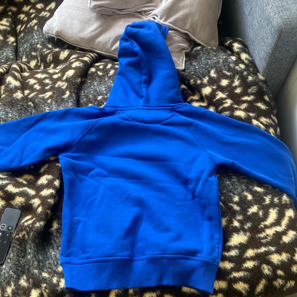 Säljer en blå hoodie från GANT med deras klassiska logga och texten 'American Sportswear' på framsidan. Tröjan har en stor ficka framtill och en bekväm huva. Perfekt för en avslappnad stil.Har använt den en gång och har ett litet hål i sig.Är i 140 barn size.. Hupparit & Collegepaidat.