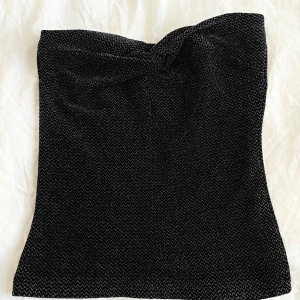 Svart glittrig tubtopp - Svart glittrig tubtopp. Perfekt för en kväll ute. Toppen har en åtsittande passform och är axelbandslös, vilket ger en stilren look🤍