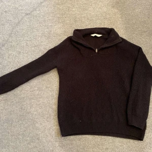 Svart stickad tröja med dragkedja - Säljer en stilren svart stickad tröja med dragkedja vid halsen. Tröjan har långa ärmar och en ribbad struktur som ger en klassisk look. Perfekt för kyligare dagar.