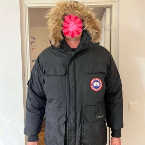 Svart dunjacka från Canada Goose - Säljer en svart dunjacka från Canada Goose med pälskantad huva. Jackan har en broderad logotyp på bröstet och flera praktiska fickor. Perfekt för kalla vinterdagar. (Defekt)🖤