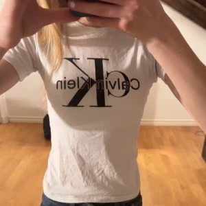 Vit t-shirt från Calvin Klein - Säljer en klassisk vit t-shirt från Calvin Klein med det ikoniska CK-logotypen tryckt i svart på framsidan. T-shirten har en normal passform och korta ärmar, perfekt för en avslappnad stil. Tillverkad i mjuk bomull för extra komfort. Tröjan är bara använd ett fåtal gånger och har inga skador eller fläckar. På bilderna är tröjan lite skrynklig men stryker innan jag skickar iväg, tyvärr är tröjan för liten och kommer inte till användning😢 jag som är 164 cm lång kan fof har den men är lite tajt💓🙏🏼💝😍